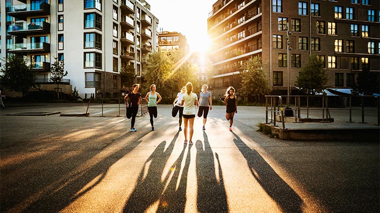 A fitness instructor talking to her class outdoors in the city.