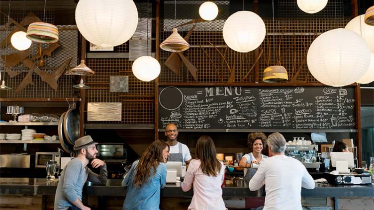 People at a cafe sitting at the bar counter and staff serving coffees - food service concepts