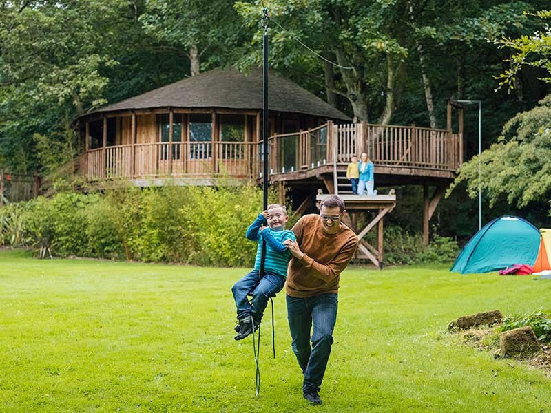 A father is playing with his kid in garden(his wife and daughter behind him)