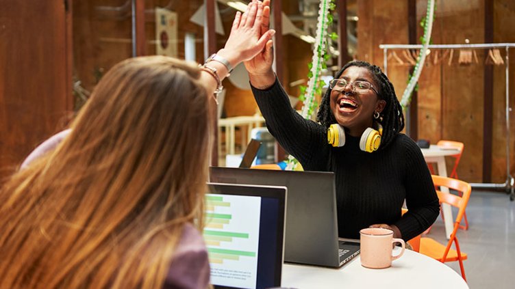 Professionals collaborate on laptops and share a celebratory high five
