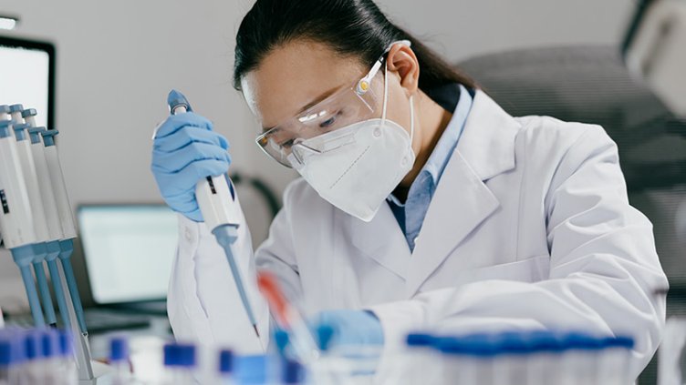 A female scientist in a lab coat and mask conducts an experiment with a test tube in a laboratory environment.