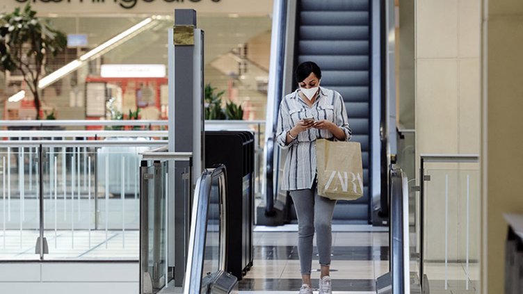 Woman coming down after shopping from escalator while using her phone in a shopping mall