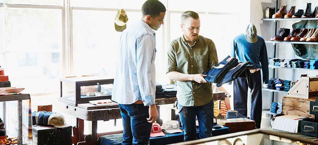 Shop owner explaining the difference in denim jeans to customer in store