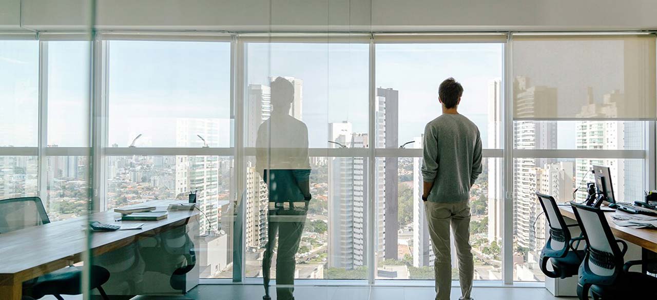 young man looks out of office window over city